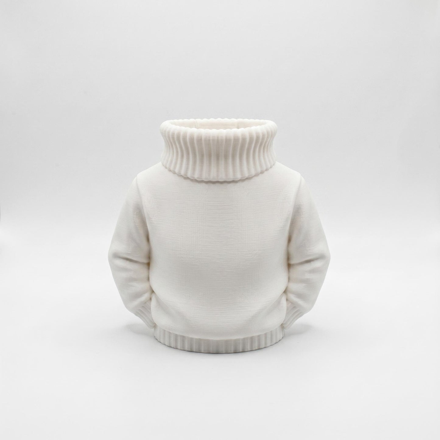 Ein charmanter weißer Stiftehalter im Pullover-Design aus 3D-Druck steht vor grauem Hintergrund. Der Organizer hat die Form eines Rollkragenpullovers mit geripptem Kragen und Saum sowie glatten Ärmeln an den Seiten. Die matte weiße PLA-Oberfläche zeigt feine Druckstrukturen. Perfekt als Schreibtisch Organizer, Abschiedsgeschenk Lehrerin oder Erzieherin. Maße 11x10x7 cm. Ideal für Büro-Deko und als originelles Schulgeschenk.