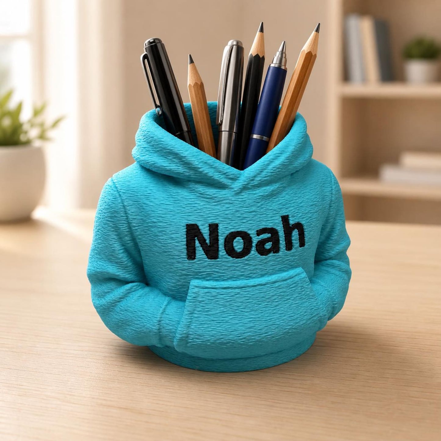 Türkisfarbener personalisierter Hoodie-Stiftehalter mit dem Namen Noah und Stiften auf hellem Schreibtisch