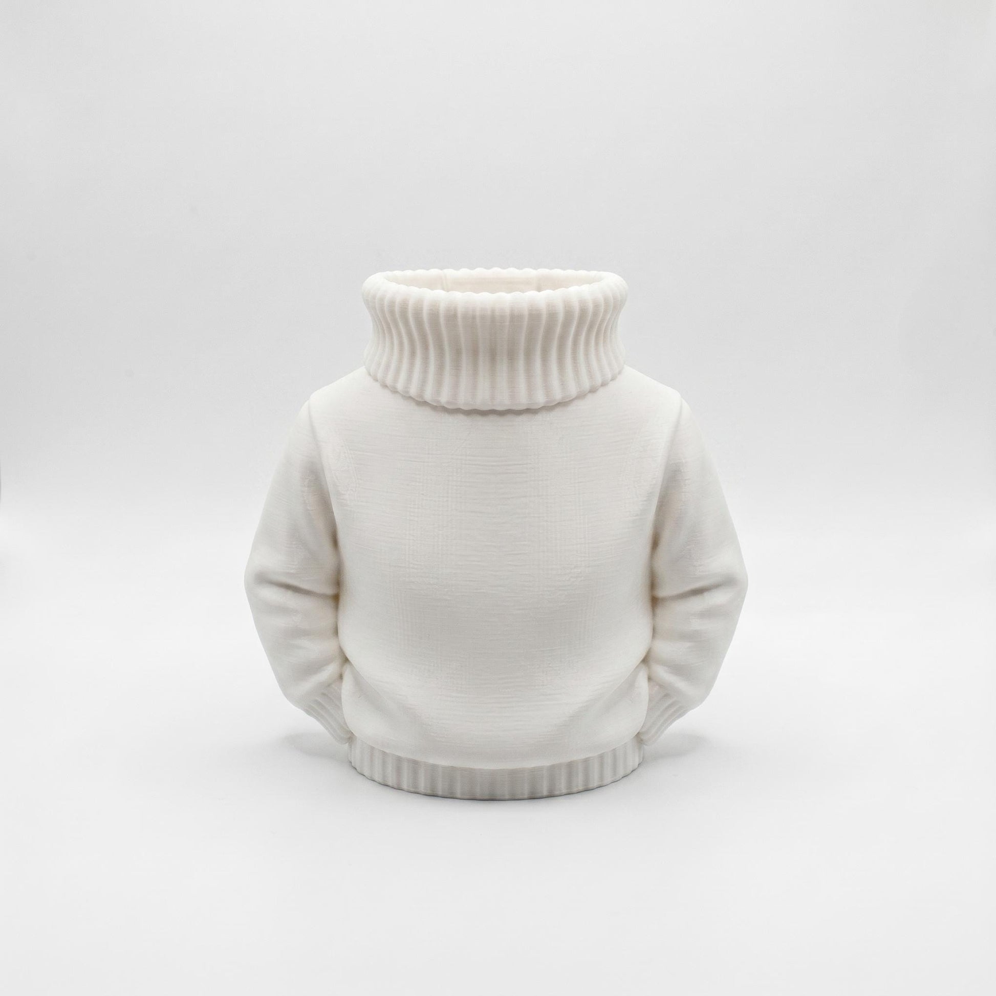 Ein charmanter weißer Stiftehalter im Pullover-Design aus 3D-Druck steht vor grauem Hintergrund. Der Organizer hat die Form eines Rollkragenpullovers mit geripptem Kragen und Saum sowie glatten Ärmeln an den Seiten. Die matte weiße PLA-Oberfläche zeigt feine Druckstrukturen. Perfekt als Schreibtisch Organizer, Abschiedsgeschenk Lehrerin oder Erzieherin. Maße 11x10x7 cm. Ideal für Büro-Deko und als originelles Schulgeschenk.