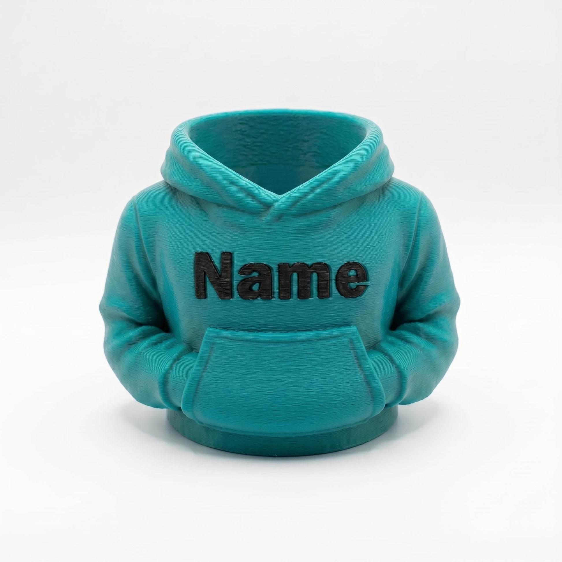 Ein türkisfarbener 3D-gedruckter Stiftehalter in Form eines Miniatur-Hoodies mit der Aufschrift Name auf der Brust. Der detailgetreue Desk Organizer zeigt realistische Hoodie-Strukturen mit Kapuze und Bauchtasche. Perfektes Abschiedsgeschenk für Lehrerin oder Erzieherin, individuell personalisierbar. Maße 11x10x7 cm, aus hochwertigem PLA-Material. Idealer Schreibtisch Organizer für Stifte und kleine Büroartikel. Auch als Schulgeschenk oder Mitgebsel geeignet.
