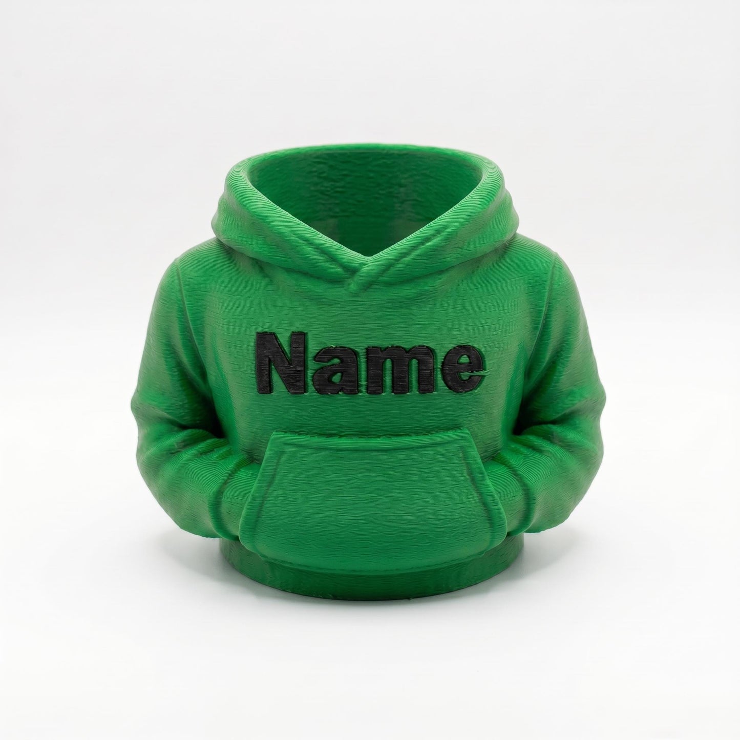 3D-gedruckter Stiftehalter in grüner Hoodie-Form mit schwarzem Name Schriftzug auf der Brust. Der detaillierte Organizer zeigt realistische Kapuze, Kängurutasche und Ärmel mit sichtbaren Drucklinien. Perfekt als Abschiedsgeschenk Lehrerin, Schulgeschenk oder Schreibtisch Organizer. Maße 11×10×7 cm, aus grünem PLA im 3D Druck hergestellt. Ideal für Einschulung oder als personalisierte Büro-Deko.