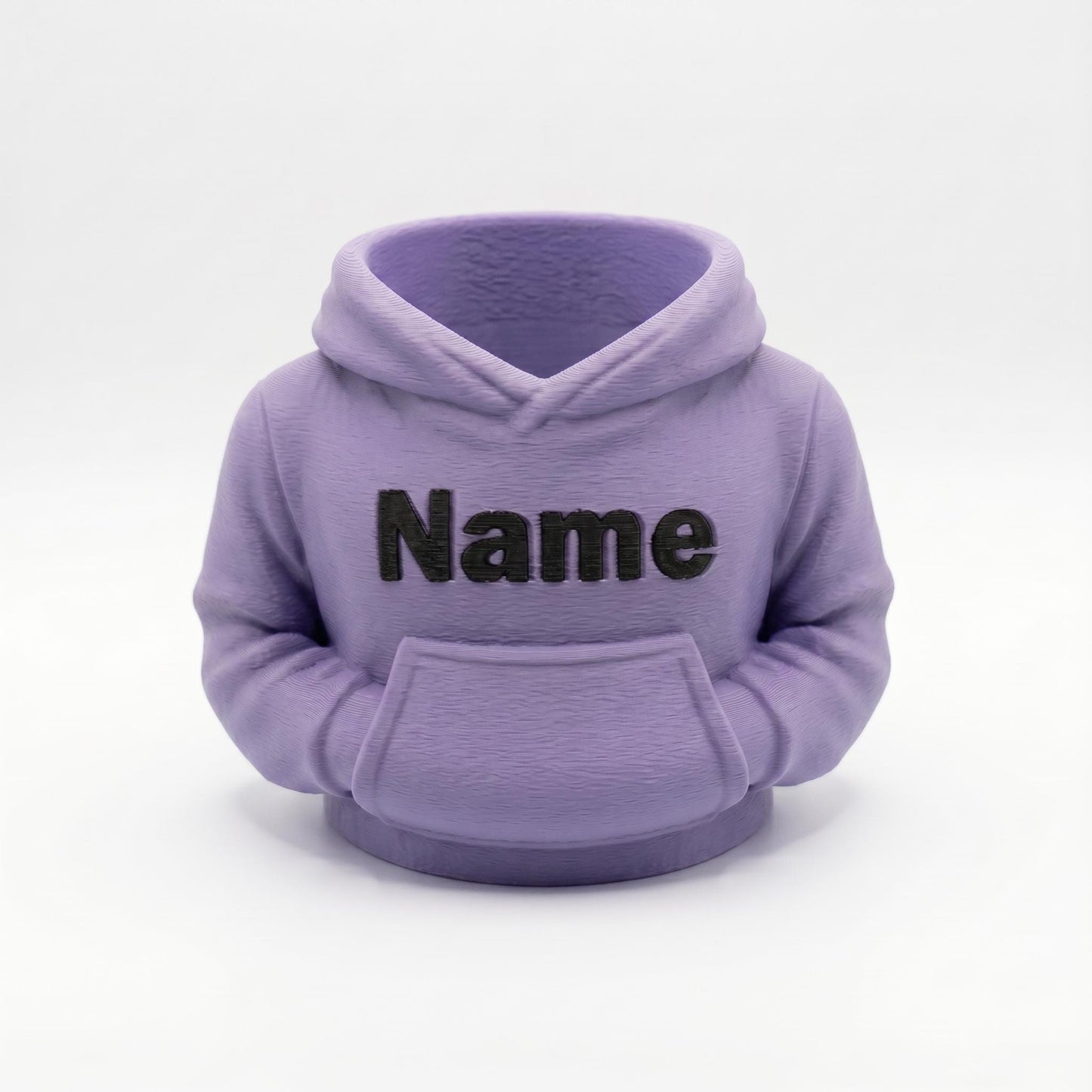 Ein 3D-gedruckter Stiftehalter in Form eines Hoodies in matter Lavendel-Farbe mit schwarzem Name-Schriftzug auf der Vorderseite. Der kompakte Organizer verfügt über eine Kapuze und Kängurutasche, perfekt als Schreibtisch-Deko. Ideales Abschiedsgeschenk für Lehrerin oder Erzieherin, Schulgeschenk oder Mitgebsel. Aus robustem PLA-Material im 3D-Druck hergestellt. Personalisierbar für individuelle Gestaltung.