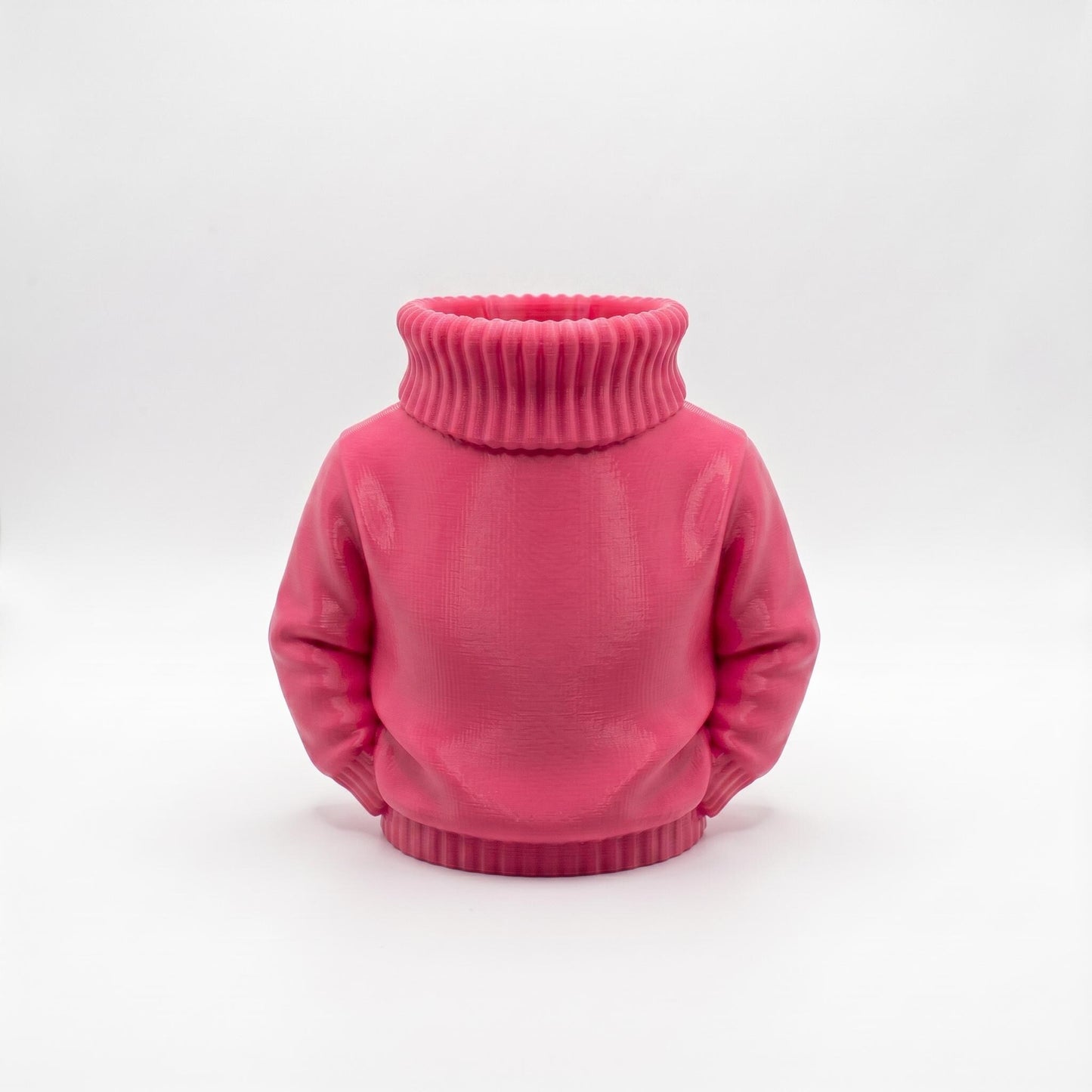 Ein rosa 3D-gedruckter Stiftehalter in Form eines Rollkragenpullovers steht vor hellgrauem Hintergrund. Das Objekt zeigt einen realistischen Pullover ohne Kopf mit charakteristischem geripptem Rollkragen und Ärmeln. Die Oberfläche weist eine matte pinke Farbe mit sichtbaren Drucklinien auf. Der hohle Halsbereich dient als Stifthalter. Perfekter Schreibtisch Organizer und originelles Abschiedsgeschenk für Lehrerin oder Erzieherin. Maße 11×10×7 cm aus PLA im 3D Druck hergestellt.