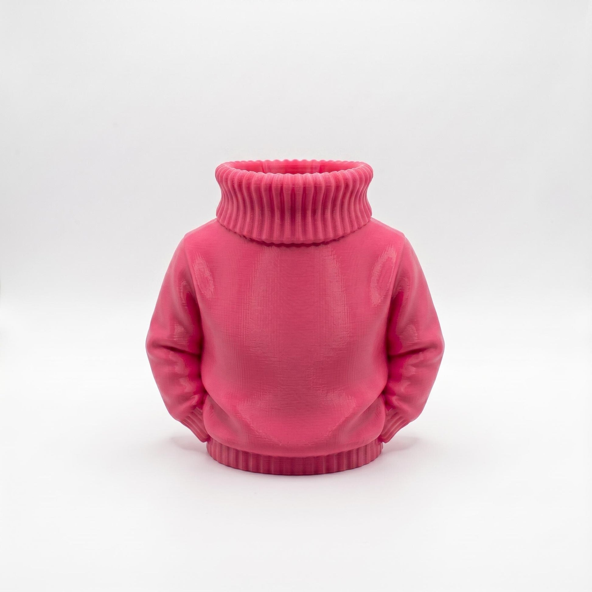 Ein rosa 3D-gedruckter Stiftehalter in Form eines Rollkragenpullovers steht vor hellgrauem Hintergrund. Das Objekt zeigt einen realistischen Pullover ohne Kopf mit charakteristischem geripptem Rollkragen und Ärmeln. Die Oberfläche weist eine matte pinke Farbe mit sichtbaren Drucklinien auf. Der hohle Halsbereich dient als Stifthalter. Perfekter Schreibtisch Organizer und originelles Abschiedsgeschenk für Lehrerin oder Erzieherin. Maße 11×10×7 cm aus PLA im 3D Druck hergestellt.