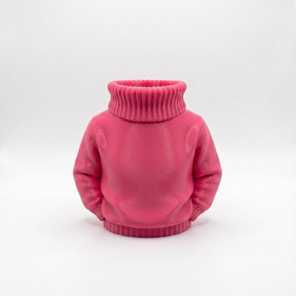 Ein rosa 3D-gedruckter Stiftehalter in Form eines Rollkragenpullovers steht vor hellgrauem Hintergrund. Das Objekt zeigt einen realistischen Pullover ohne Kopf mit charakteristischem geripptem Rollkragen und Ärmeln. Die Oberfläche weist eine matte pinke Farbe mit sichtbaren Drucklinien auf. Der hohle Halsbereich dient als Stifthalter. Perfekter Schreibtisch Organizer und originelles Abschiedsgeschenk für Lehrerin oder Erzieherin. Maße 11×10×7 cm aus PLA im 3D Druck hergestellt.