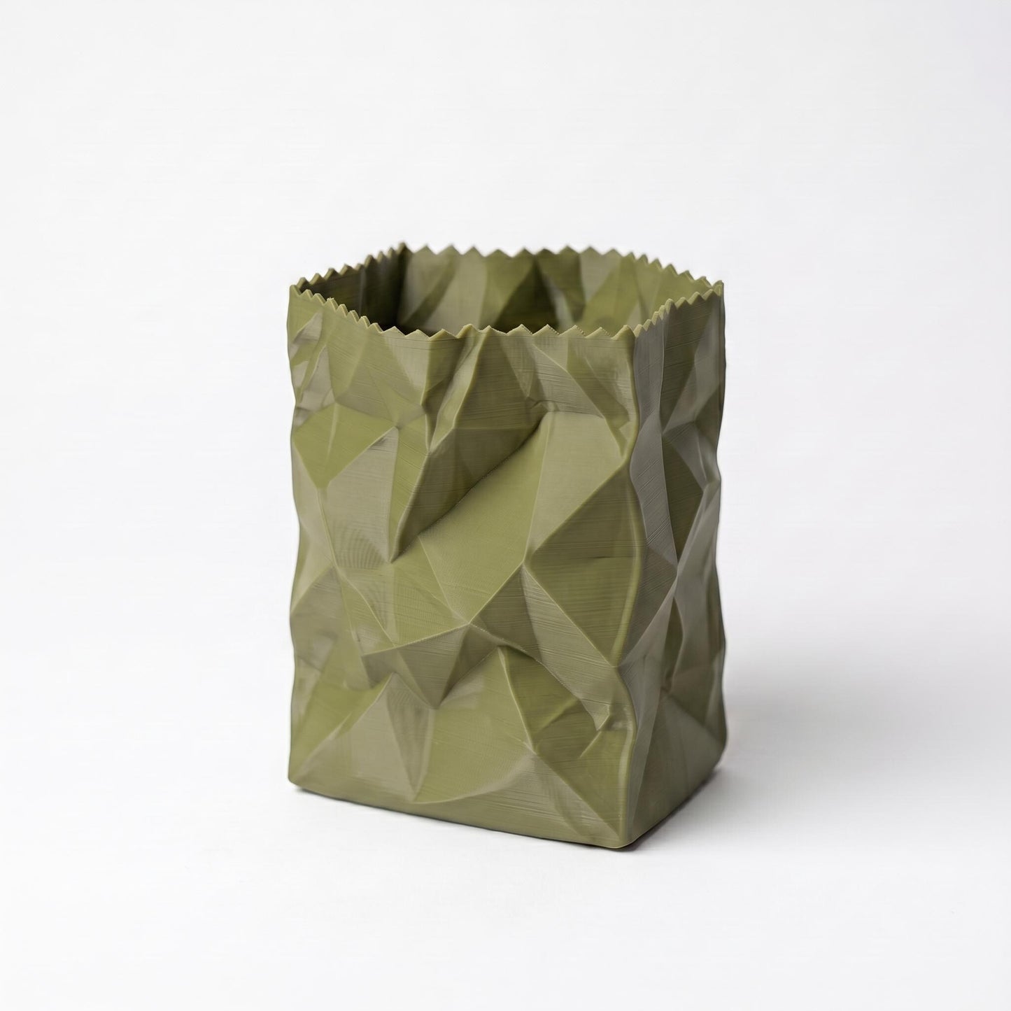 Ein olivgrüner 3D-gedruckter Stiftehalter im zerknüllten Papiertüten-Design steht vor weißem Hintergrund. Die geometrischen Falten und Kanten erzeugen eine realistische Knitteroptik. Der moderne desk organizer aus PLA-Filament hat einen gezackten oberen Rand und bietet praktischen Stauraum für Stifte und Büroartikel. Perfekt als office desk decor oder Schulgeschenk.