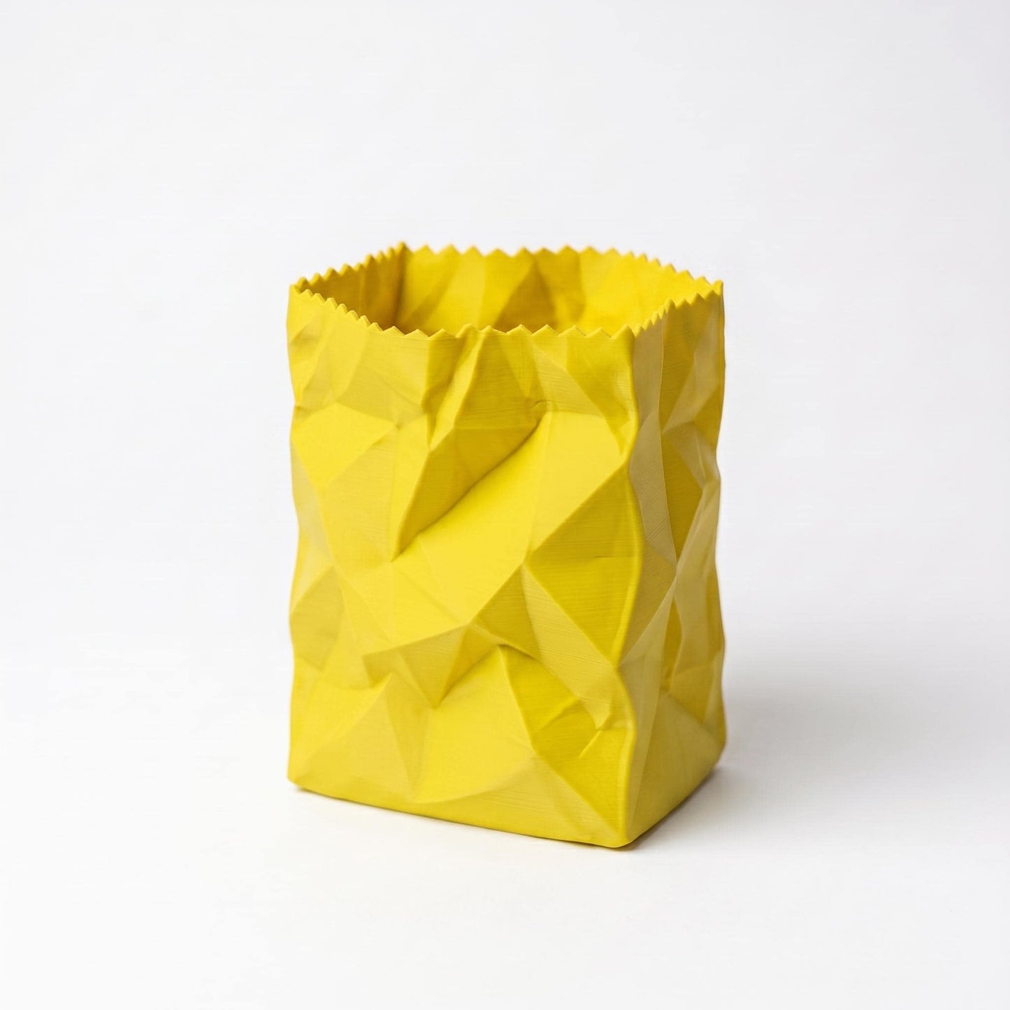 Gelber 3D-gedruckter Stiftehalter in zerknitterter Papiertüten-Optik mit geometrischen Falten und gezacktem oberen Rand. Das moderne Design verleiht jedem Schreibtisch eine spielerische Note. Perfekter desk organizer für Stifte und Büromaterial - ein echter Hingucker als office desk decor. Hochwertig aus PLA gefertigt, 10x7x7cm, in 9 Farben erhältlich.