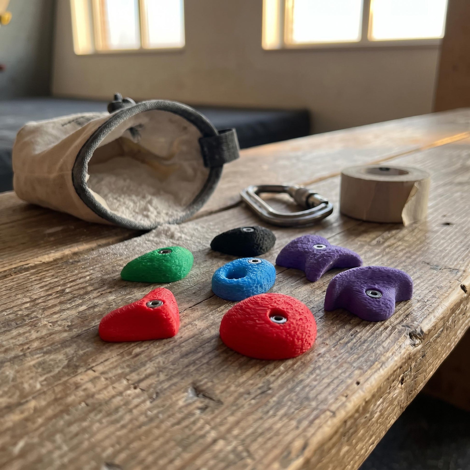 Bouldergriff-Magnete auf einer Boulderhallen-Bank neben Chalkbag, Carabiner und Klettertape — handgemachte Mini-Klettergriffe für Kletterer.