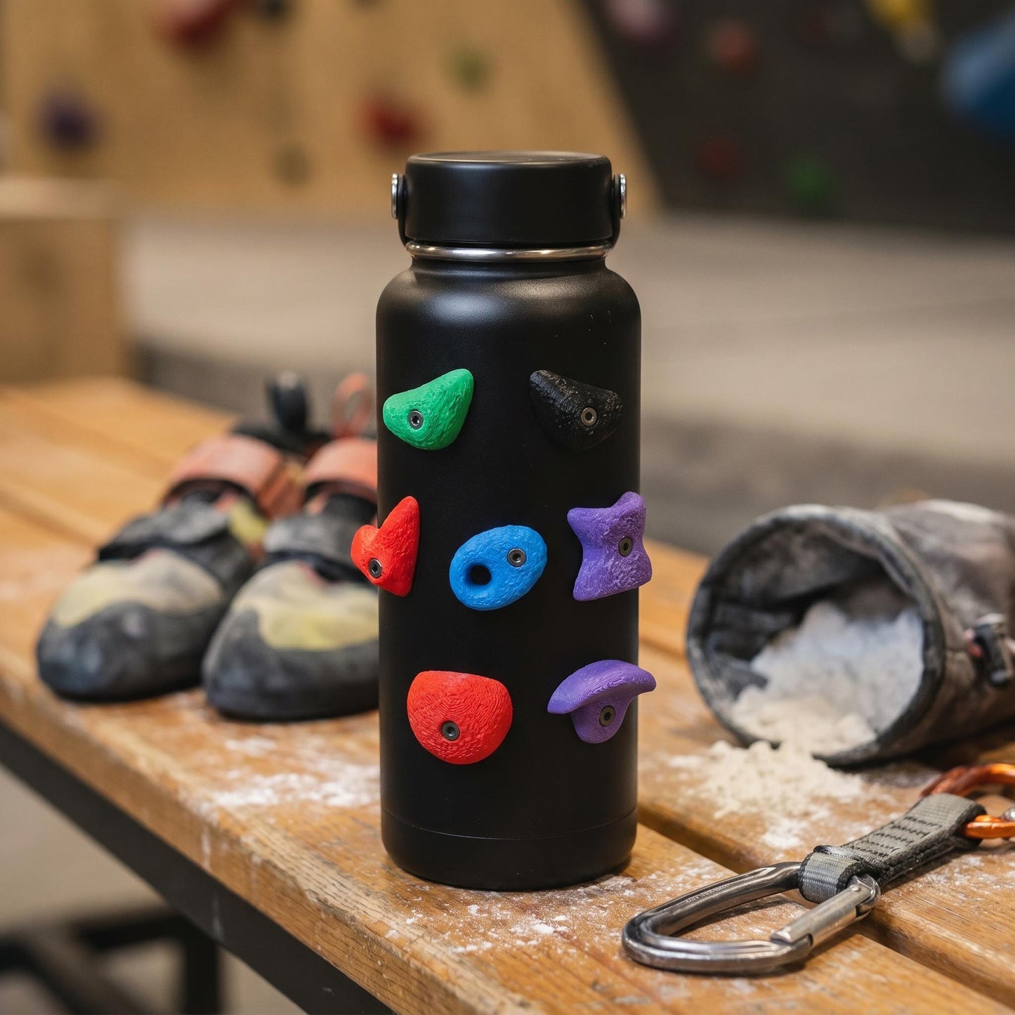 Bouldergriff-Magnete an einer schwarzen Aluminium-Trinkflasche, daneben Kletterschuhe und Chalkbag — kreatives Kletter-Gadget.