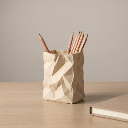Cremeweißer Stiftehalter in Papiertüten-Optik auf einem Holzschreibtisch, gefüllt mit Holzstiften