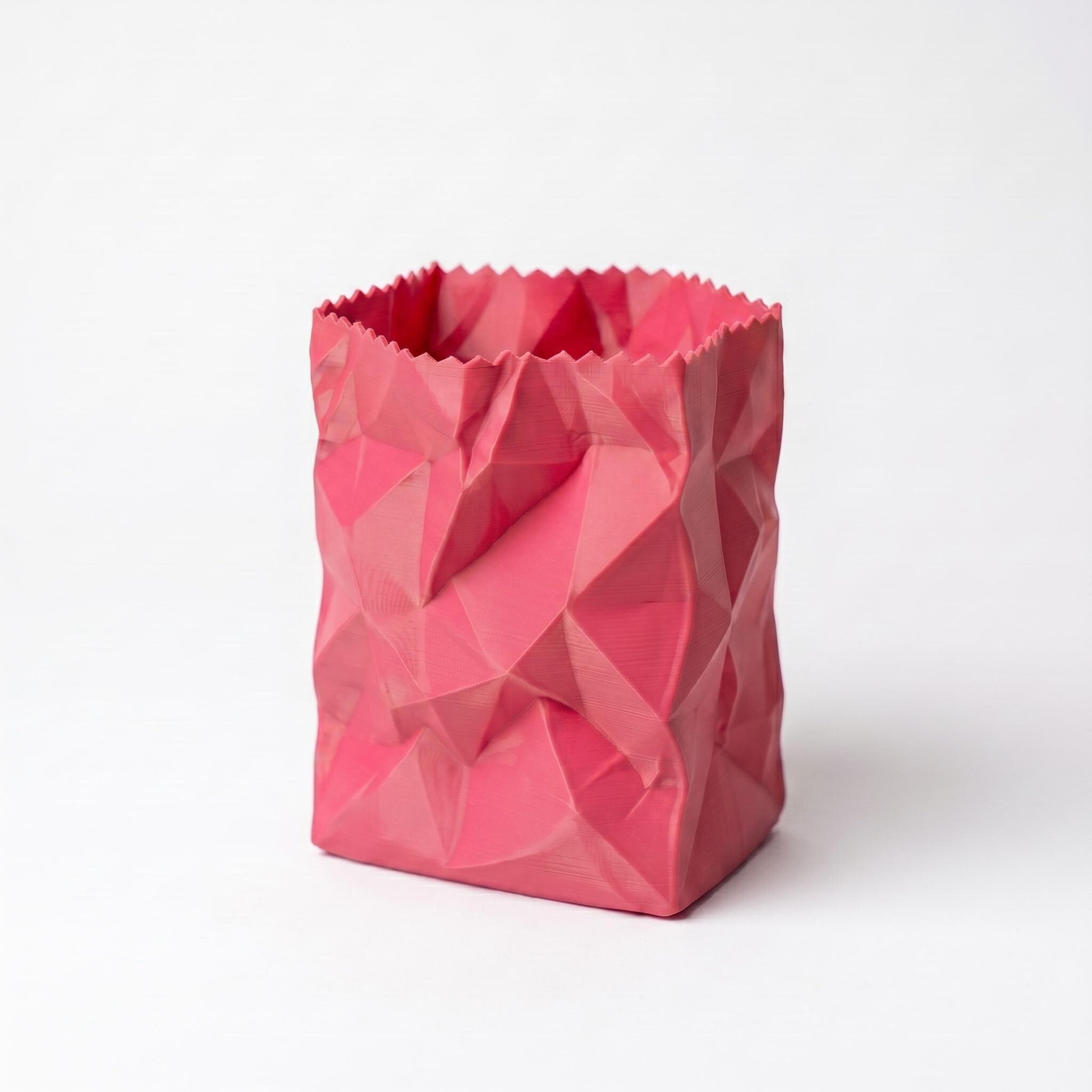 Ein pinker 3D-gedruckter Stiftehalter in zerknüllter Papiertüten-Optik mit geometrischen Facetten und gezacktem oberen Rand. Der moderne desk organizer aus PLA-Filament zeigt eine strukturierte Oberfläche mit dreieckigen Vertiefungen und eignet sich perfekt als pen holder für den Schreibtisch. Ideal als Büro-Deko oder Schulgeschenk.