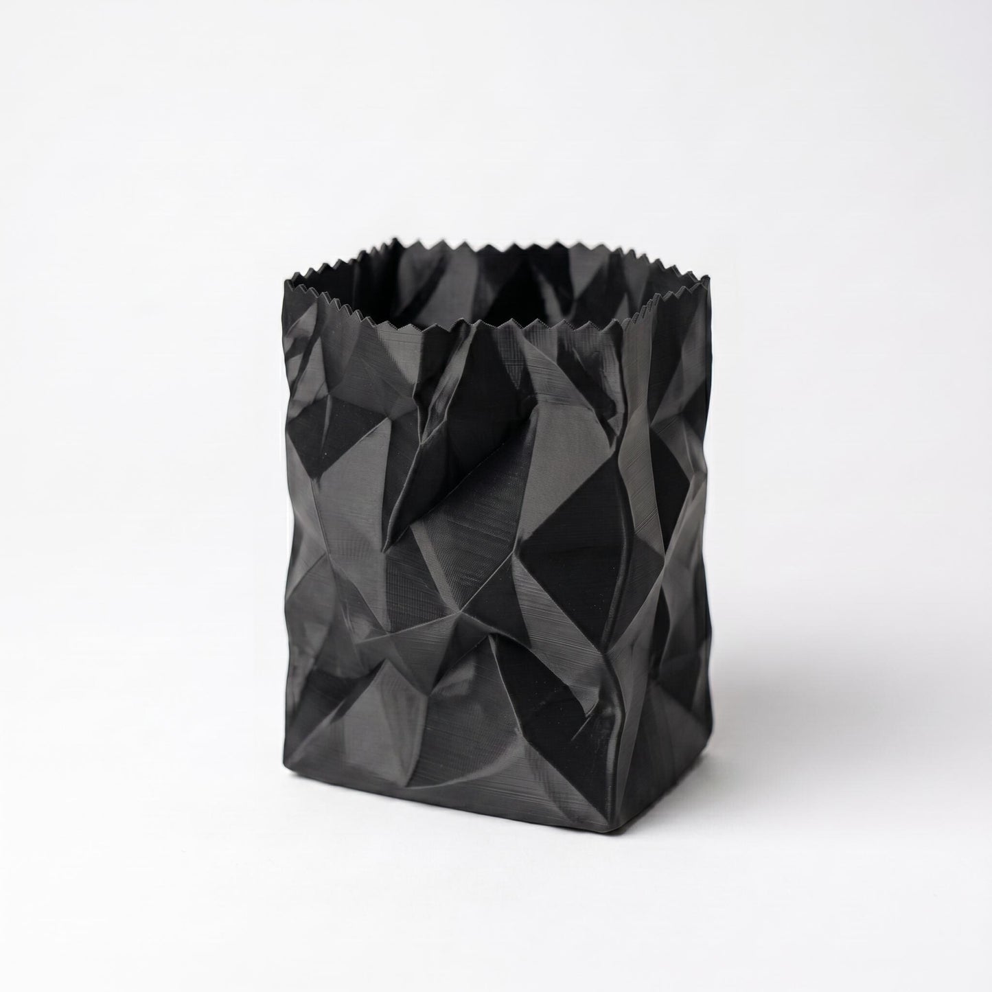 Schwarzer 3D-gedruckter Stiftehalter im zerknüllten Papiertüten-Design aus PLA-Filament. Das geometrisch facettierte Muster erzeugt eine realistische Knitteroptik mit tiefen Schatten und Falten. Perfekter desk organizer für Büro und Schreibtisch - moderner pen holder in einzigartigem crumpled paper Design. Maße: 10x7x7cm, in 9 Standardfarben erhältlich.