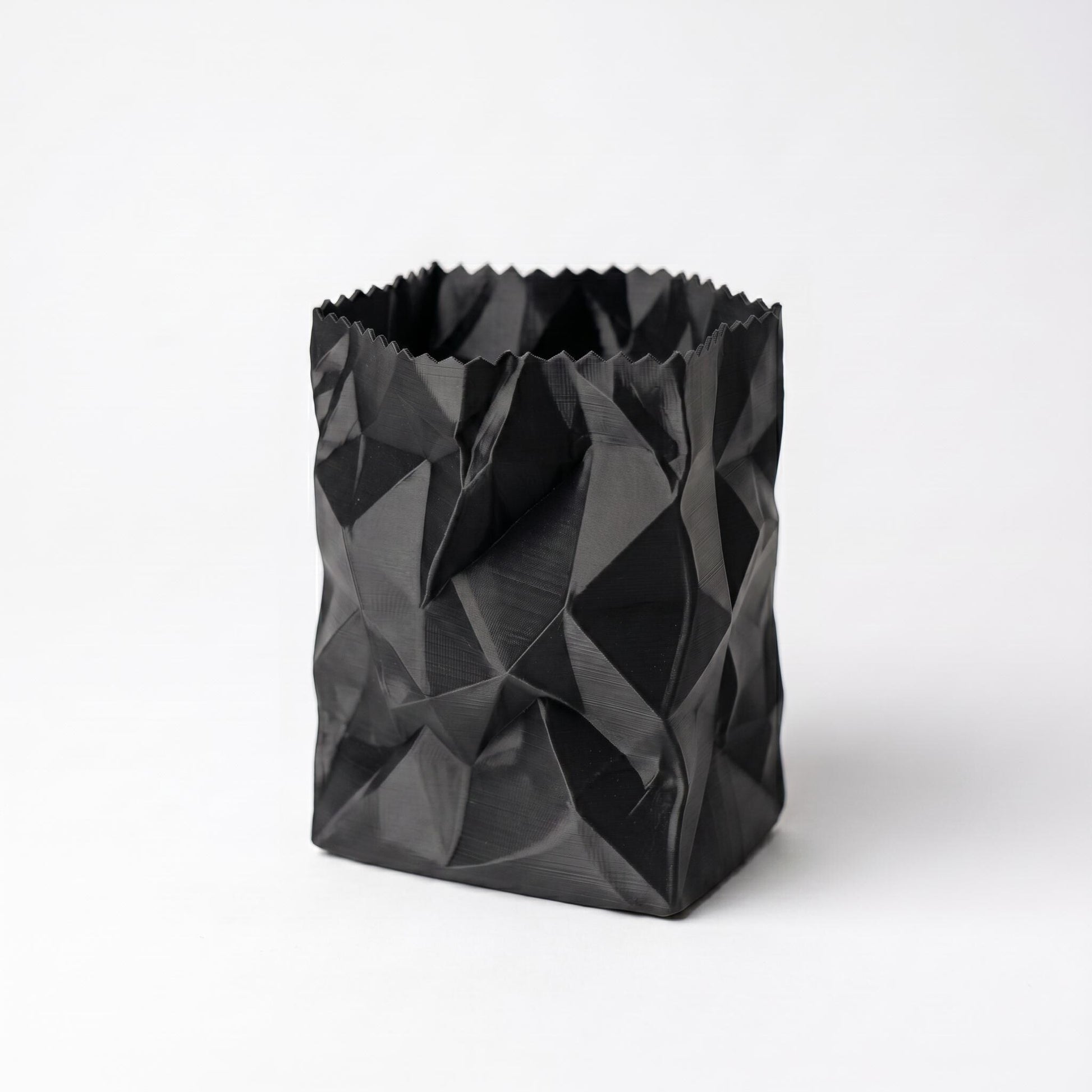 Schwarzer 3D-gedruckter Stiftehalter im zerknüllten Papiertüten-Design aus PLA-Filament. Das geometrisch facettierte Muster erzeugt eine realistische Knitteroptik mit tiefen Schatten und Falten. Perfekter desk organizer für Büro und Schreibtisch - moderner pen holder in einzigartigem crumpled paper Design. Maße: 10x7x7cm, in 9 Standardfarben erhältlich.