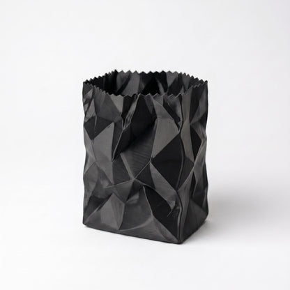 Schwarzer 3D-gedruckter Stiftehalter im zerknüllten Papiertüten-Design aus PLA-Filament. Das geometrisch facettierte Muster erzeugt eine realistische Knitteroptik mit tiefen Schatten und Falten. Perfekter desk organizer für Büro und Schreibtisch - moderner pen holder in einzigartigem crumpled paper Design. Maße: 10x7x7cm, in 9 Standardfarben erhältlich.