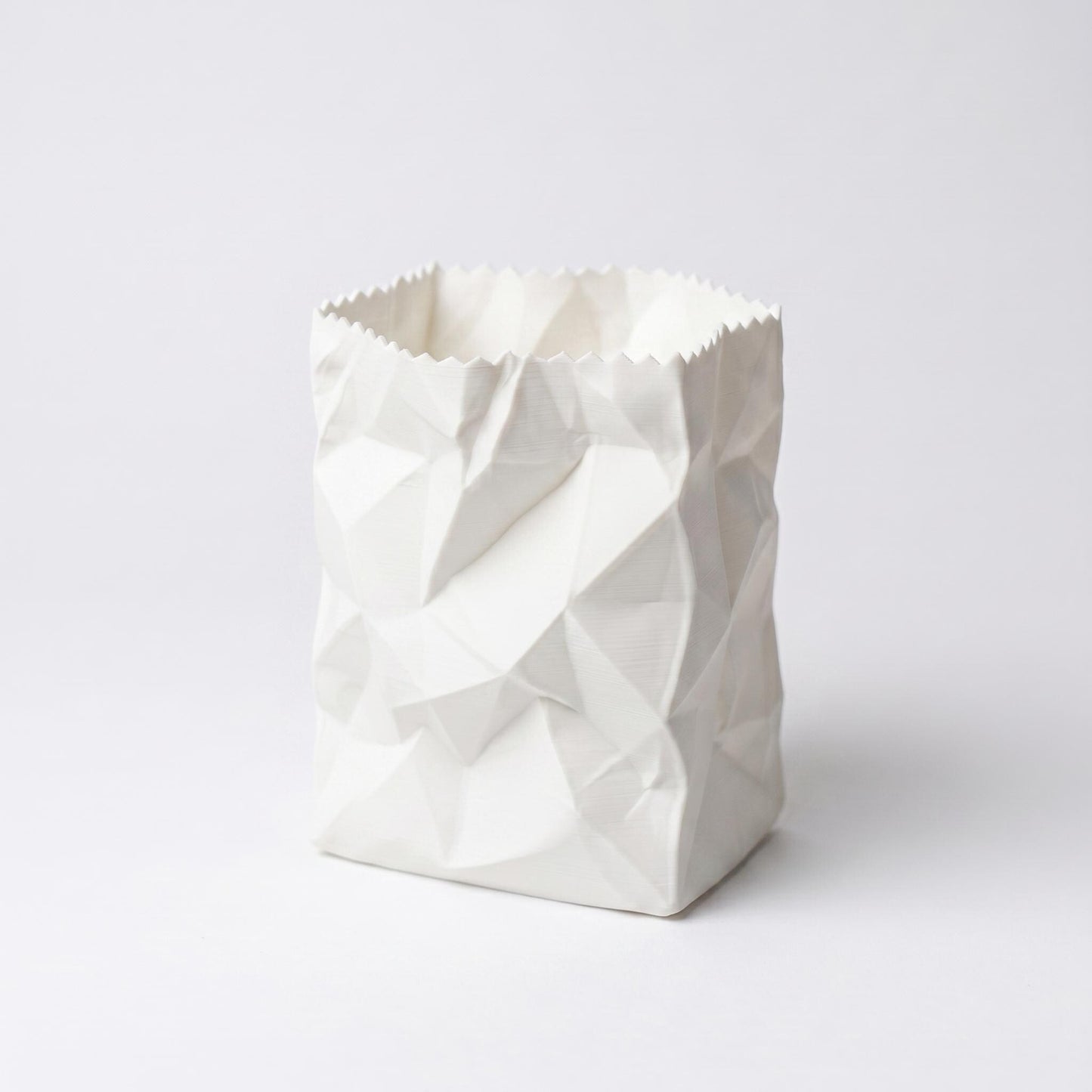 Ein weißer 3D-gedruckter Stiftehalter im Design einer zerknüllten Papiertüte auf hellem Hintergrund. Das PLA-Material zeigt realistische Falten und Knicke einer zusammengedrückten Tüte. Der Desk Organizer mit gezacktem oberen Rand ist perfekt als Pen Holder für den Schreibtisch oder als originelles Schulgeschenk geeignet.