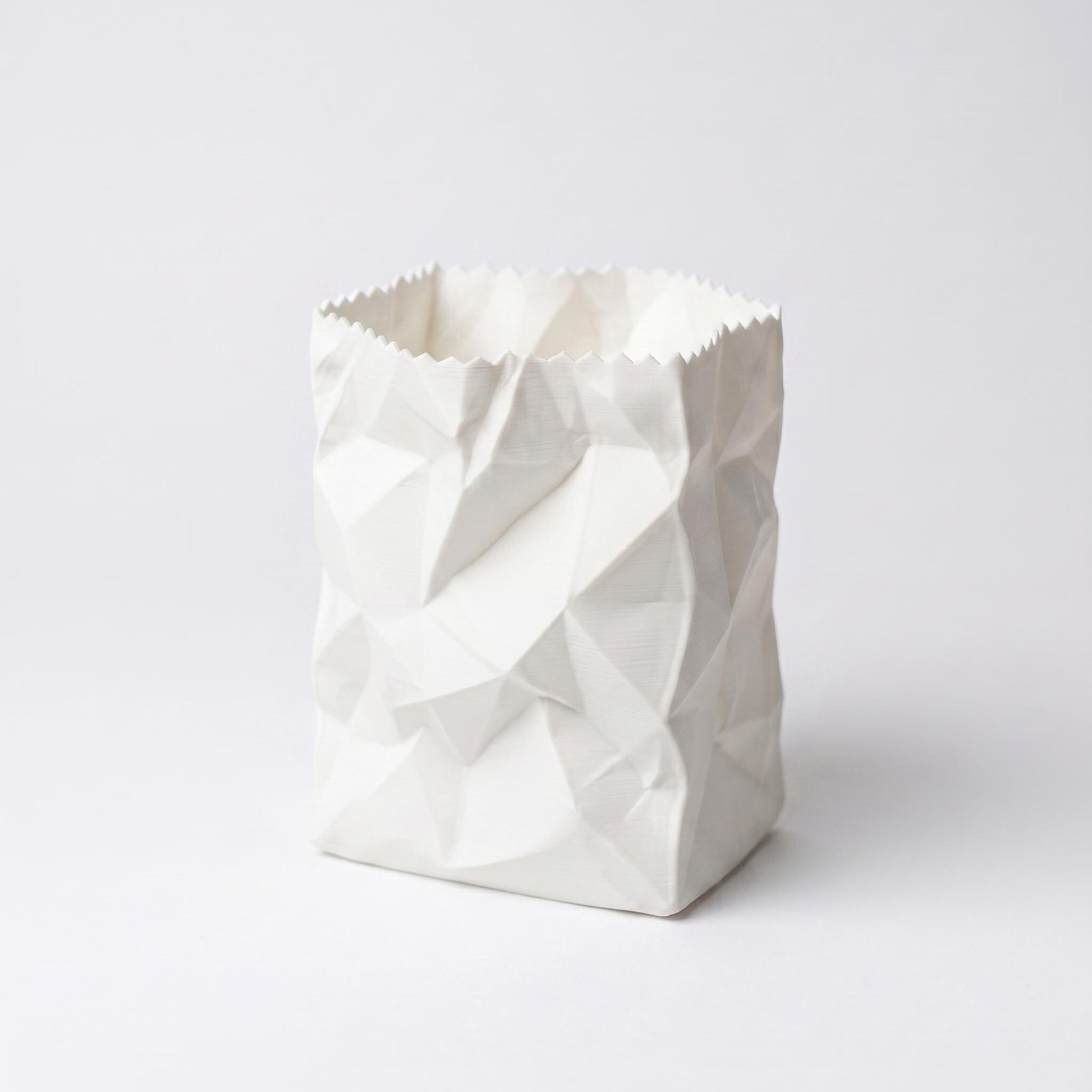 Ein weißer 3D-gedruckter Stiftehalter im Design einer zerknüllten Papiertüte auf hellem Hintergrund. Das PLA-Material zeigt realistische Falten und Knicke einer zusammengedrückten Tüte. Der Desk Organizer mit gezacktem oberen Rand ist perfekt als Pen Holder für den Schreibtisch oder als originelles Schulgeschenk geeignet.