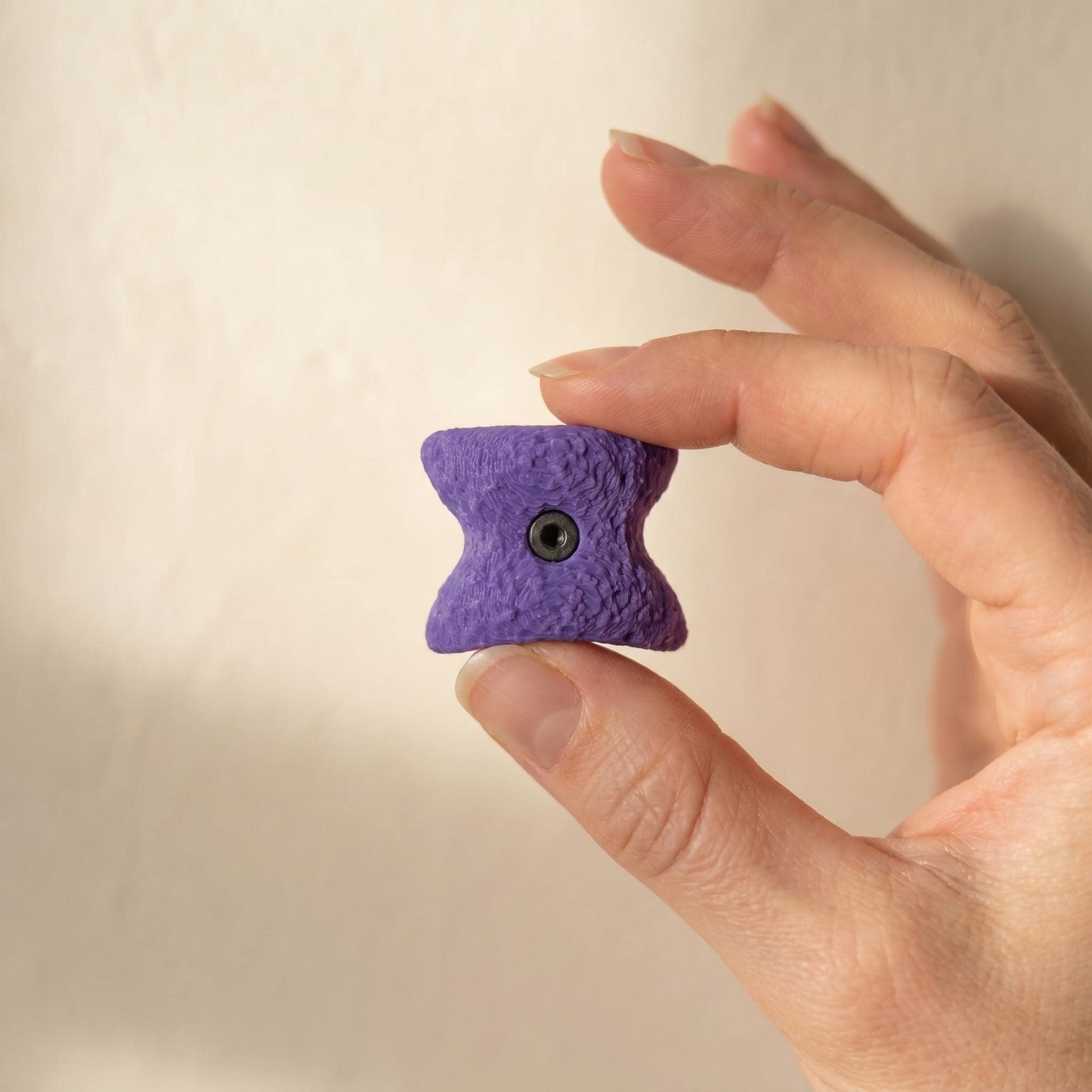 Lila Bouldergriff-Magnet zwischen Daumen und Zeigefinger — Größenvergleich: ca. 2-3 cm pro Mini-Klettergriff.