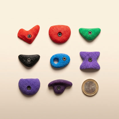 Bouldergriff-Magnete im Raster neben einer 1-Euro-Münze auf Cremehintergrund — präziser Größenvergleich für das 7er-Set.
