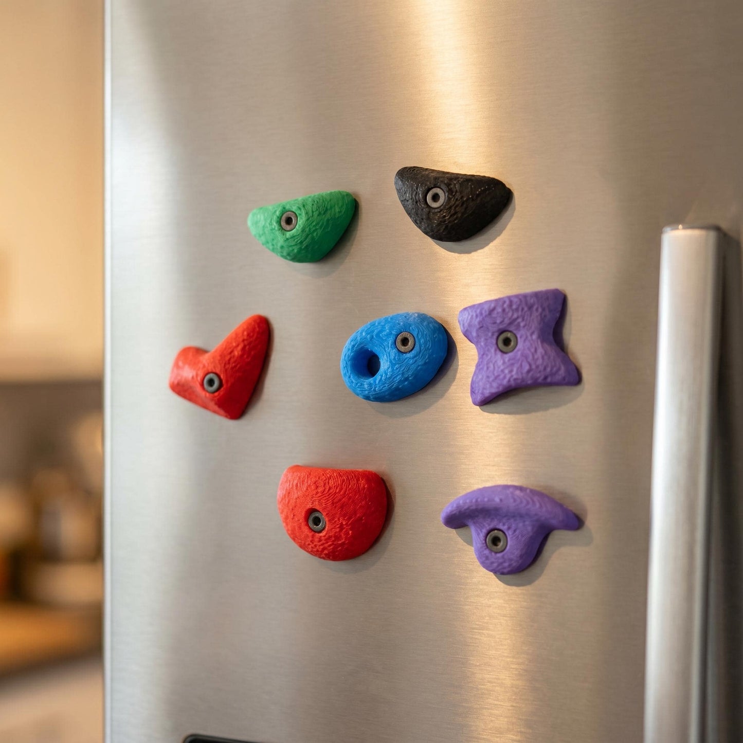 Bouldergriff-Magnete in lockerer Anordnung auf moderner Edelstahl-Kühlschranktür — minimalistischer Color-Pop als Wohn-Deko.