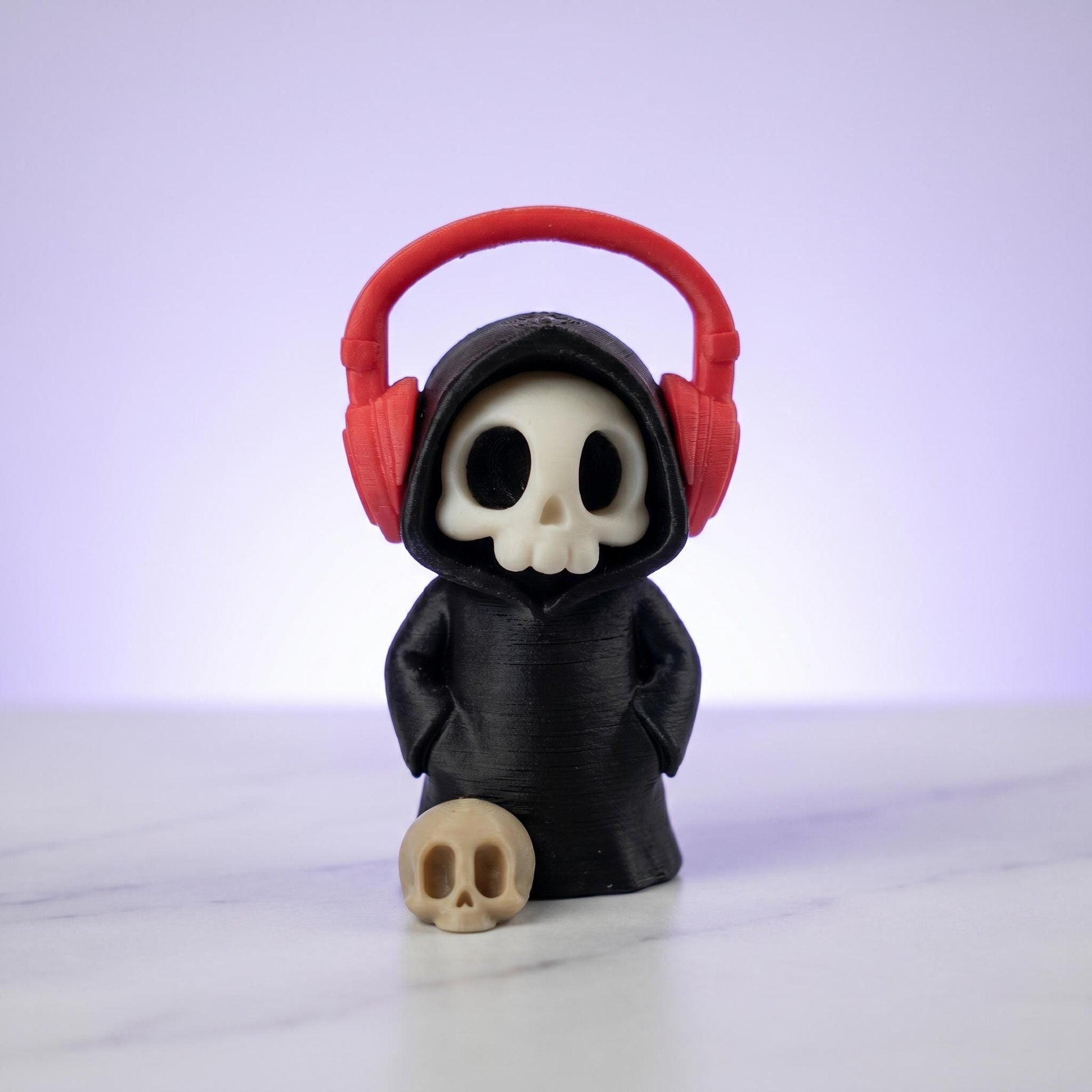 Sensenmann-Figur mit Kopfhörern und Totenkopf-Maske, davor ein Mini-Schädel – 3D-gedruckter Desk-Buddy
