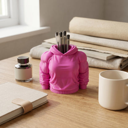 Pinker Hoodie-Stiftehalter im Muskel-Stil mit voluminösen Ärmeln neben Notizbuch und Tasse