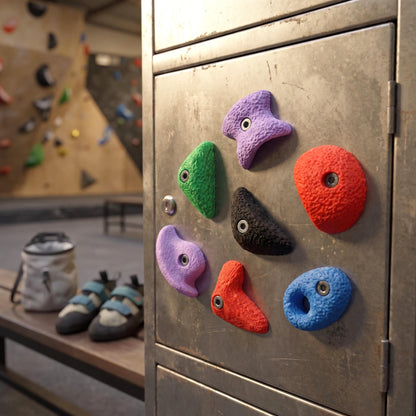 Die sieben großen Bouldergriff-Magnete an einer Metallspind-Tür in der Boulderhalle, im Hintergrund unscharf Chalkbag und Kletterschuhe. Halten auf magnetischen Stahlflächen wie Spind, Kühlschrank oder Magnettafel.