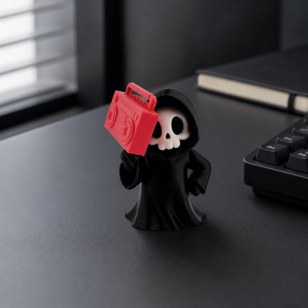 3D-gedruckte Gothic Sensenmann-Figur aus PLA mit sichtbaren feinen Druckschichten als bewusstem Teil der Oberfläche; kleine Boombox-Figur als Deko auf einem Schreibtisch.