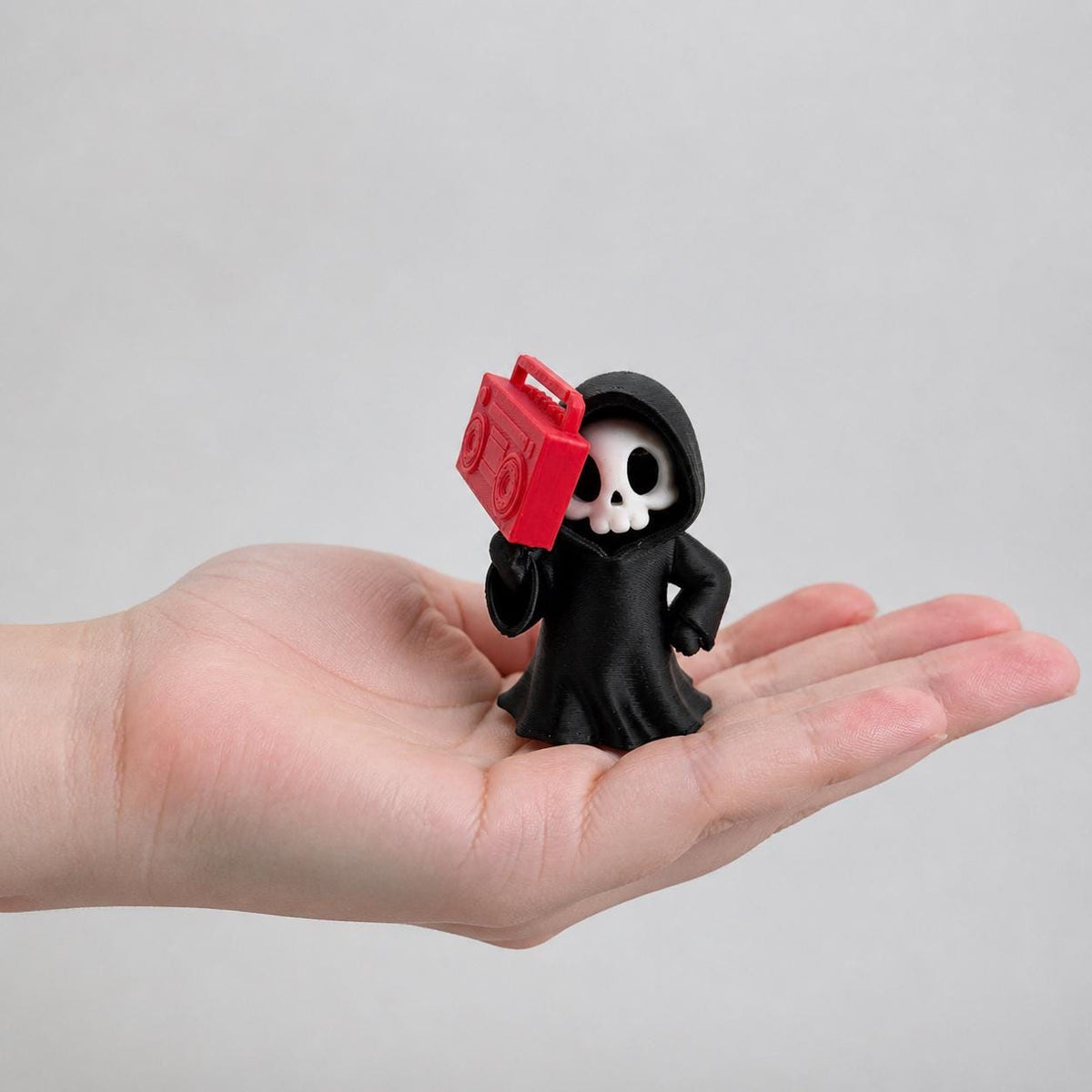 3D-gedruckte Gothic Sensenmann-Figur aus PLA mit sichtbaren feinen Druckschichten als bewusstem Teil der Oberfläche; Figur in einer erwachsenen Hand zur Größenorientierung.