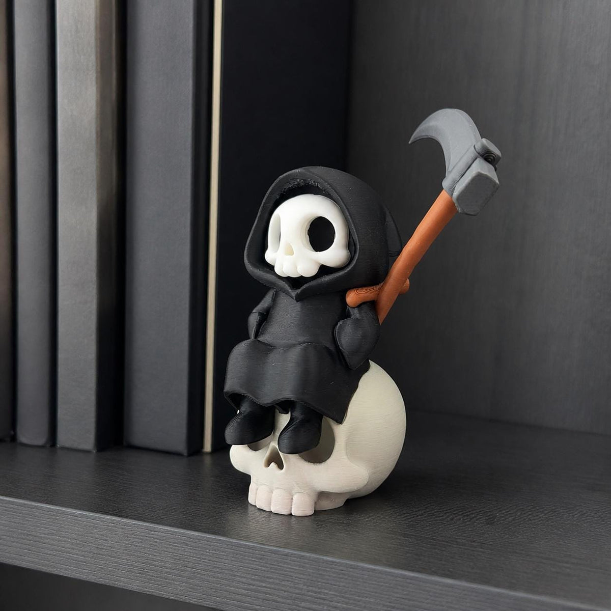 3D-gedruckte Gothic Sensenmann-Figur aus PLA mit sichtbaren feinen Druckschichten als bewusstem Teil der Oberfläche; Sensenmann auf Schädel als Deko zwischen Büchern im Regal.