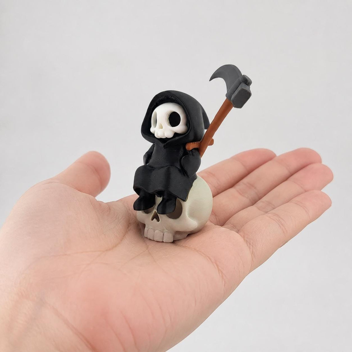 3D-gedruckte Gothic Sensenmann-Figur aus PLA mit sichtbaren feinen Druckschichten als bewusstem Teil der Oberfläche; Figur in einer erwachsenen Hand zur Größenorientierung.