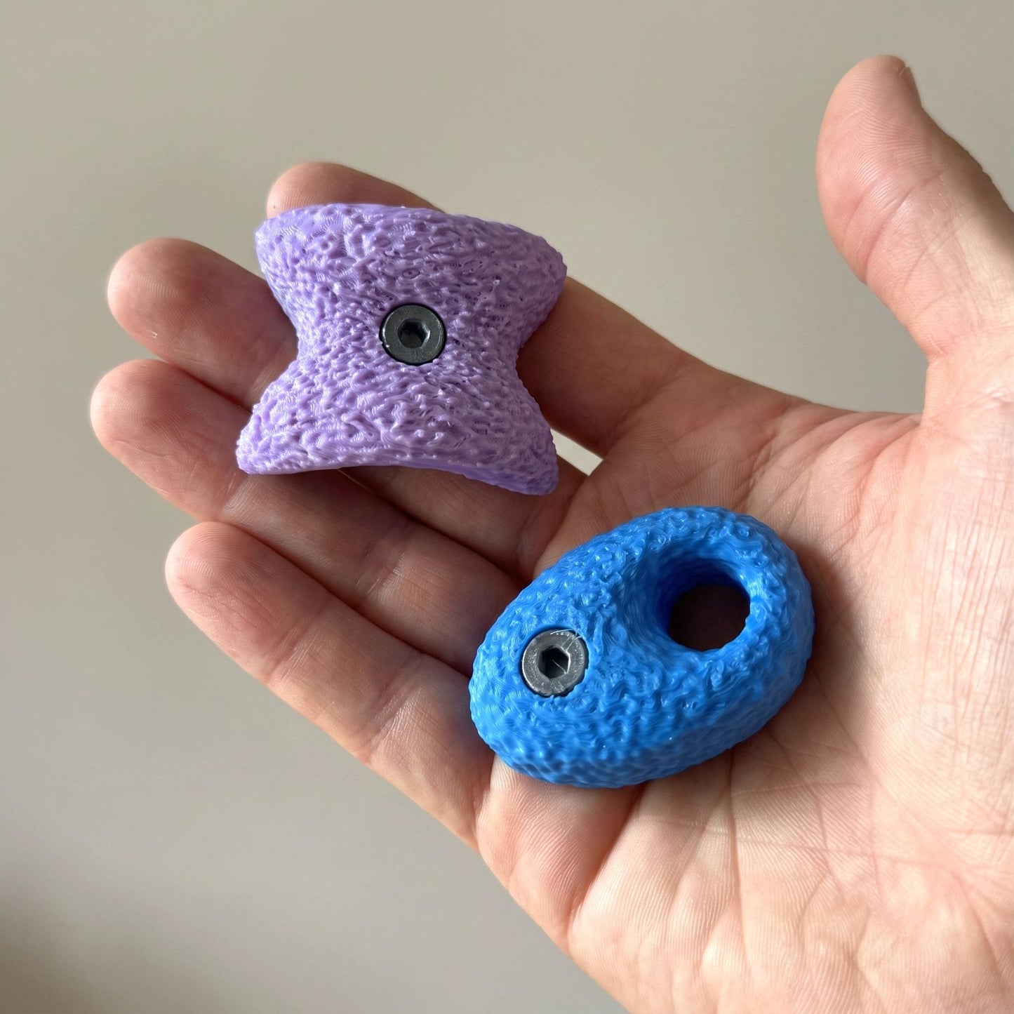 Größenvergleich aus zweiter Perspektive: fliederfarbener Bowtie und blauer Pocket in einer geöffneten Hand. Die große Variante liegt spürbar in der Hand und ist deutlich größer als eine Mini-Ausführung.