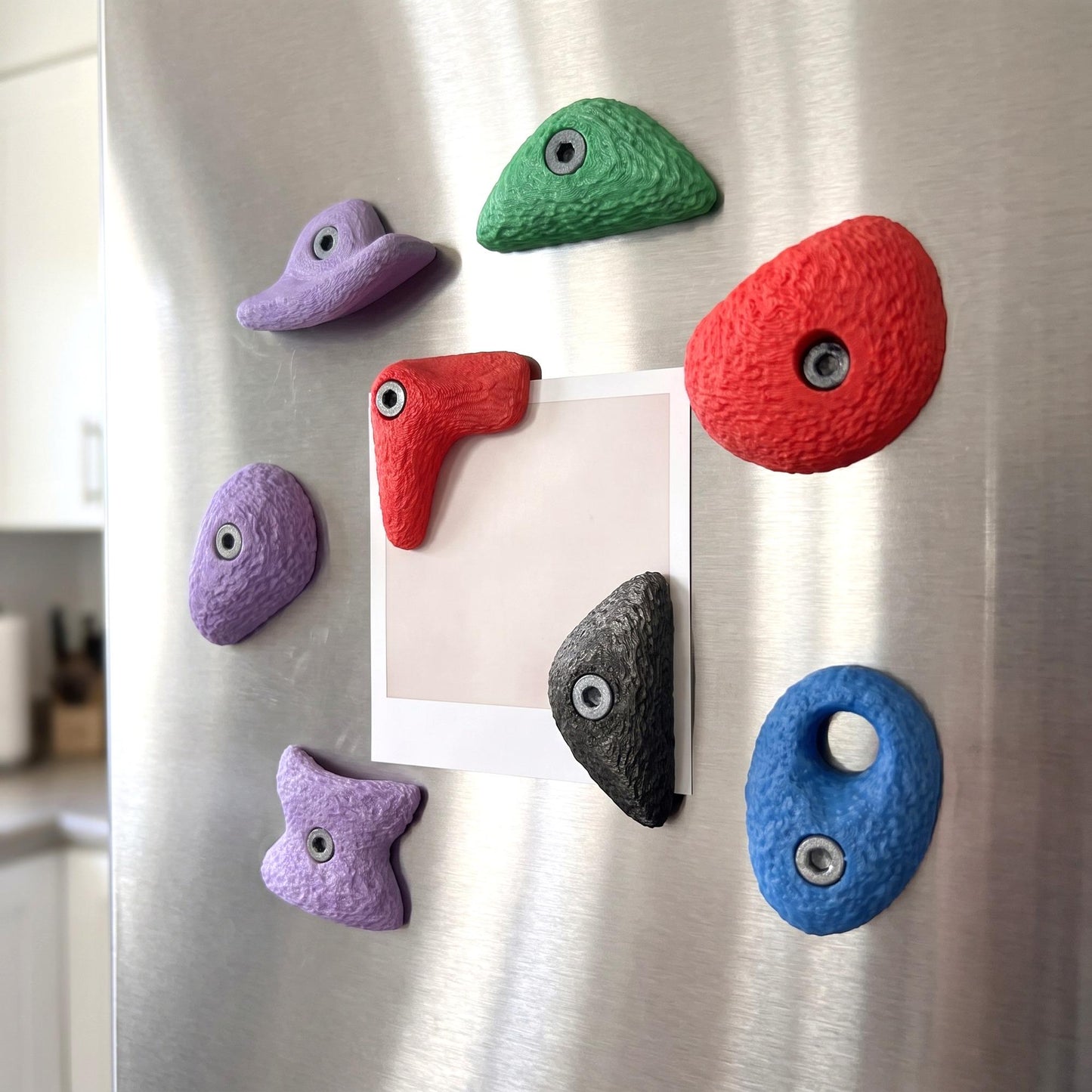 Die großen Bouldergriff-Magnete an einer Edelstahl-Kühlschranktür, zwei davon halten ein Foto. Bunte Kletter-Deko für die Küche und ein Geschenk für alle, die bouldern und klettern.