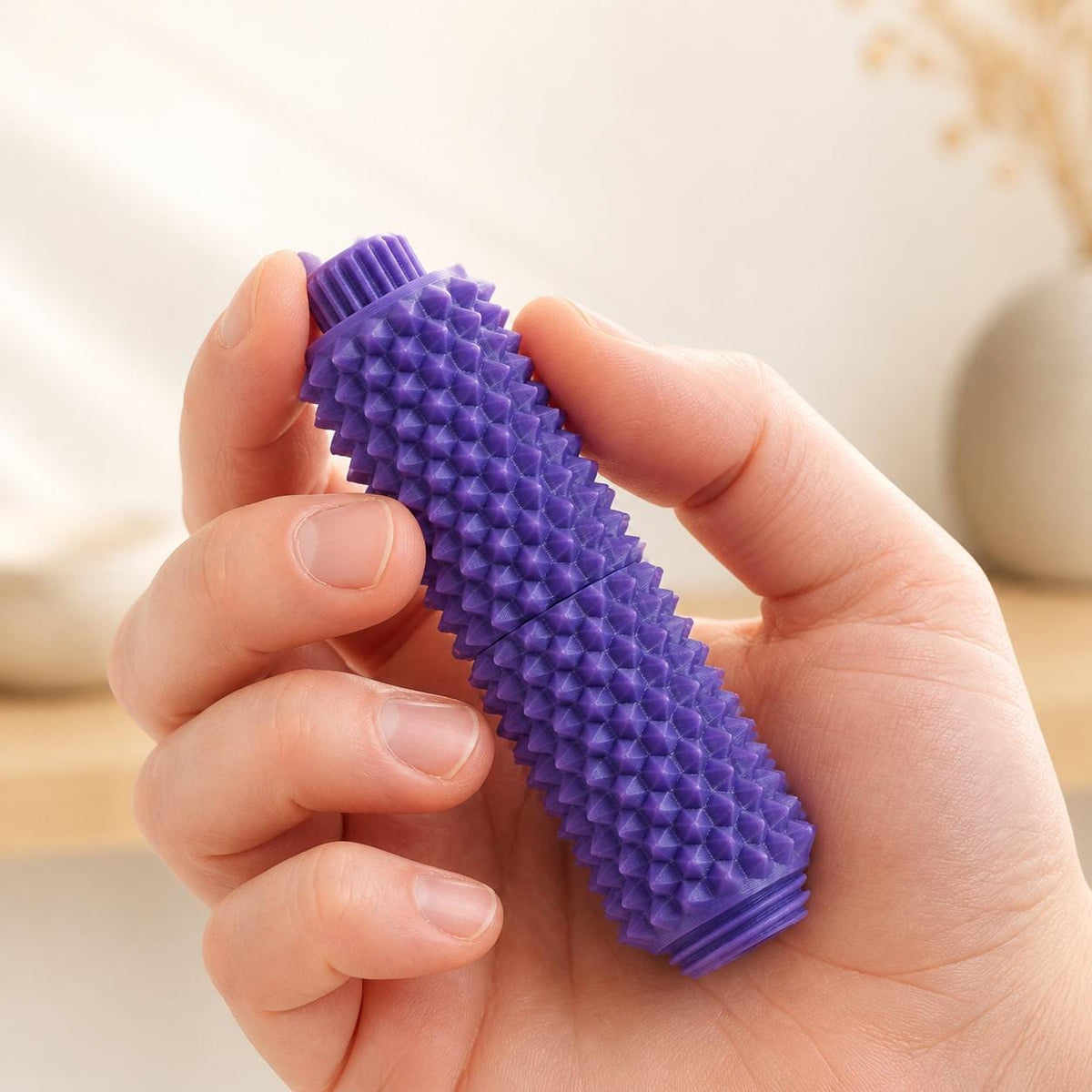 Lila Spiky Clicker Fidget Toy aus 3D-gedrucktem PLA in einer Hand. Sichtbar sind der geriffelte Drehknopf, die mittige Teilung und die stachelige Oberfläche des taktilen Anti-Stress-Spielzeugs.