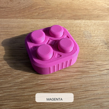 Magentafarbener 2×2 Bubble Popper mit vier runden Druckflächen, schräg von oben auf einem Holztisch fotografiert.
