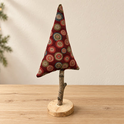 Handgenähter roter Stoff-Tannenbaum auf Naturast und Holzscheibe vor hellem, warmem Hintergrund.