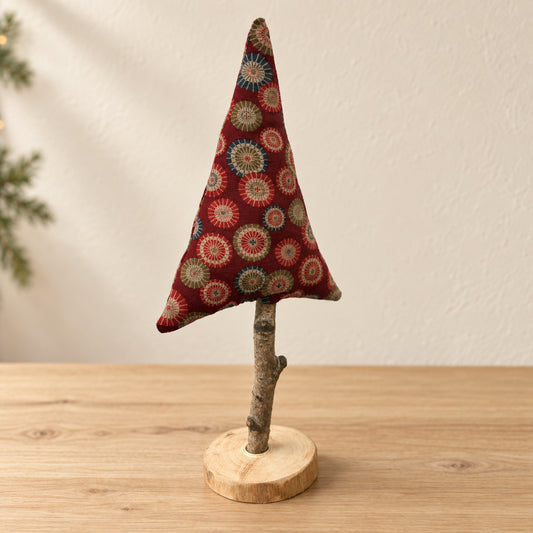 Handgenähter roter Stoff-Tannenbaum auf Naturast und Holzscheibe vor hellem, warmem Hintergrund.