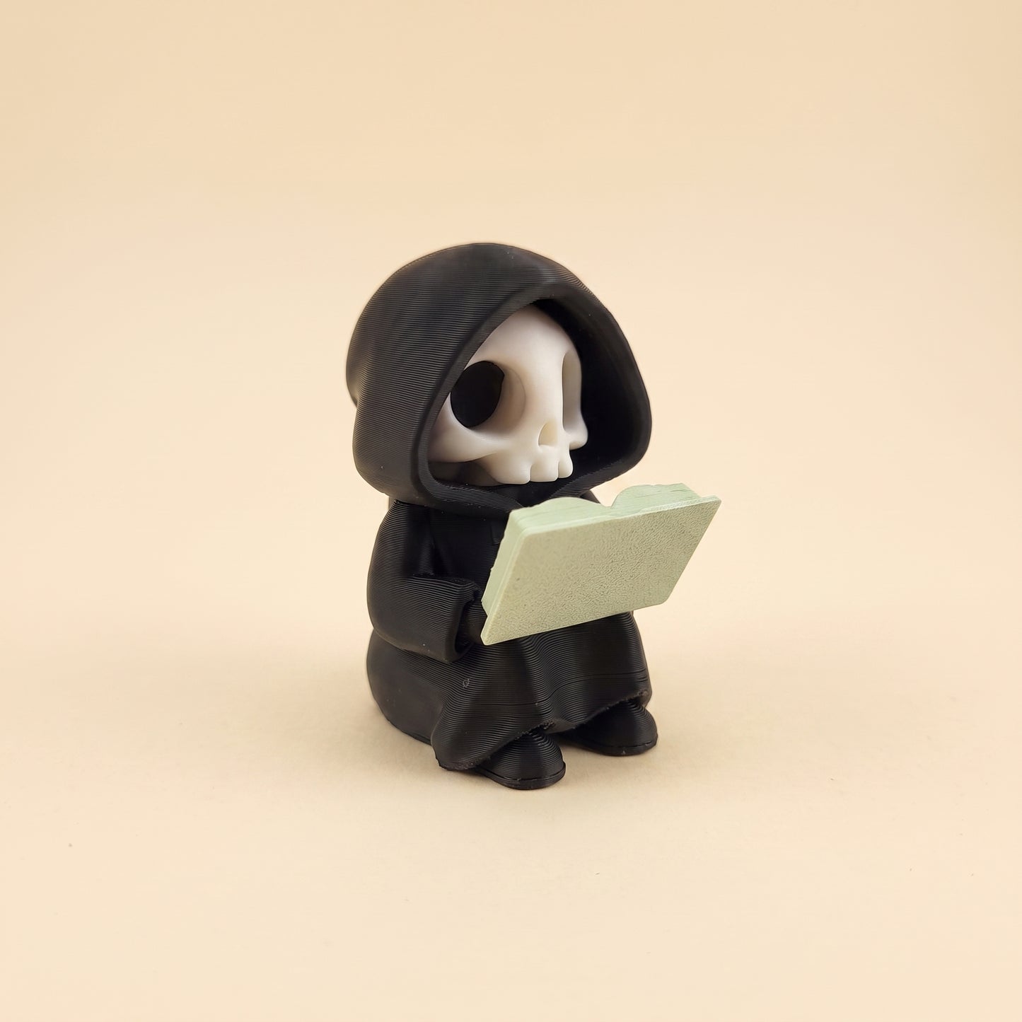 Lesender Sensenmann auf Buch – Figur fürs Bücherregal – Produktfoto auf Creme-Hintergrund