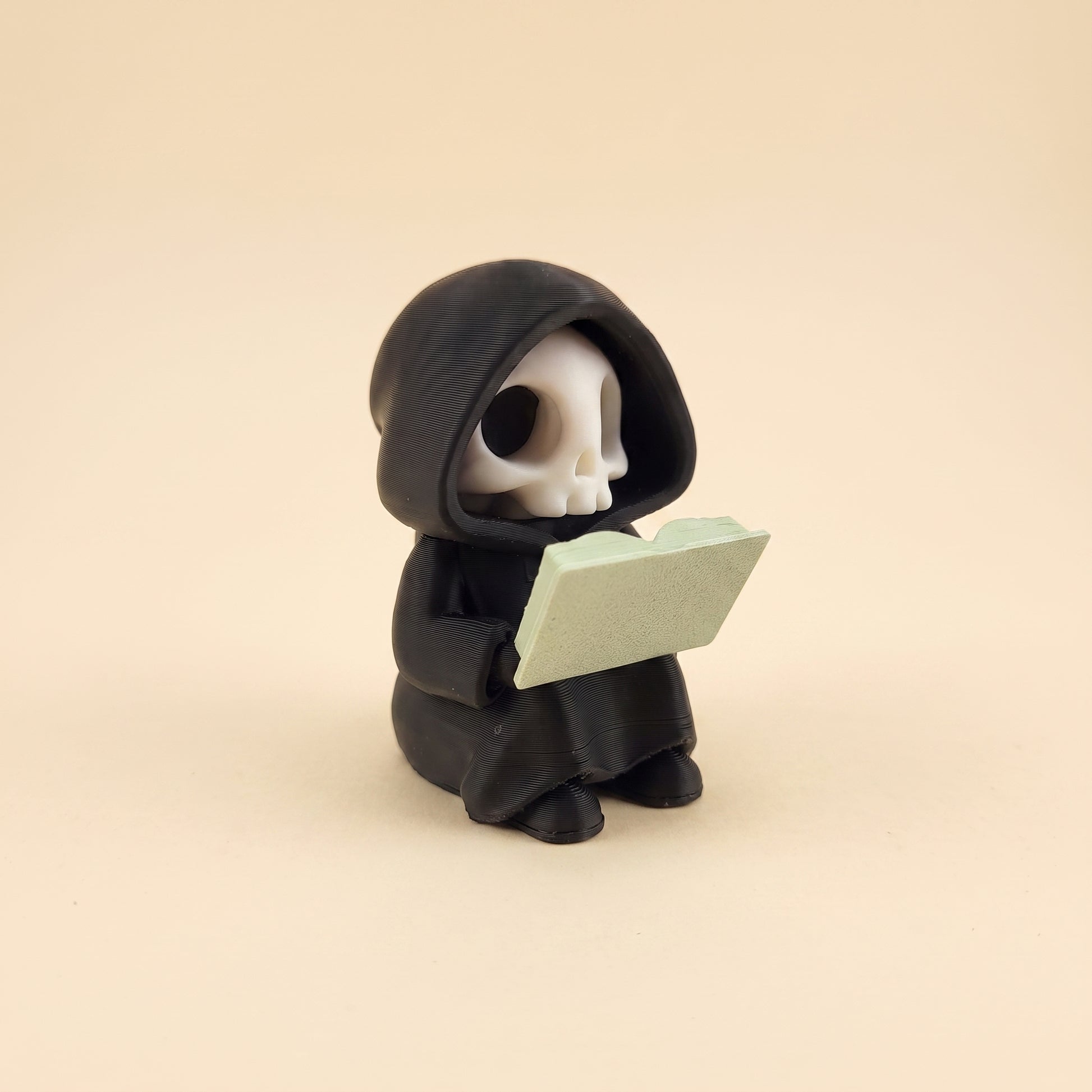 Lesender Sensenmann auf Buch – Figur fürs Bücherregal – Produktfoto auf Creme-Hintergrund