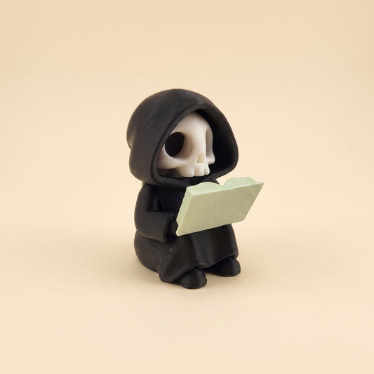 Lesender Sensenmann auf Buch – Figur fürs Bücherregal – Produktfoto auf Creme-Hintergrund